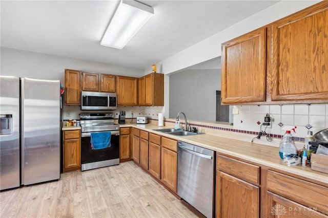 kitchen featuring brown cabinetry, a sink, light countertops, appliances with stainless steel finishes, and light wood-type flooring