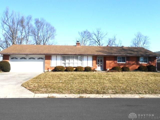 ranch-style house featuring a front lawn, driveway, a garage, brick siding, and a chimney