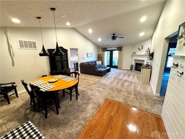 carpeted dining space featuring baseboards, visible vents, a fireplace, vaulted ceiling, and a textured ceiling