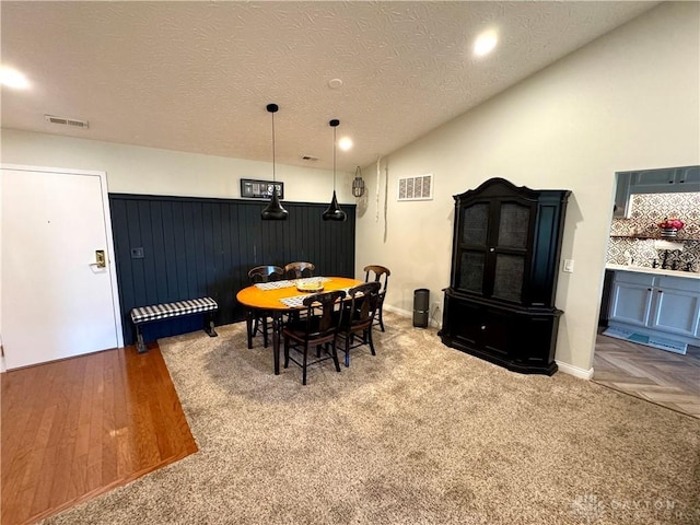 dining room with visible vents, a textured ceiling, wood finished floors, and vaulted ceiling