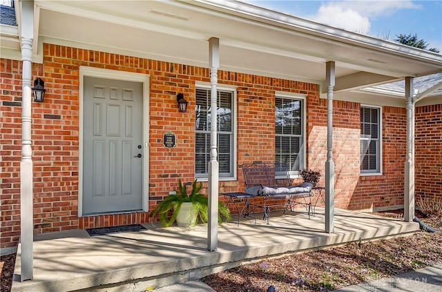 view of exterior entry featuring brick siding and a porch