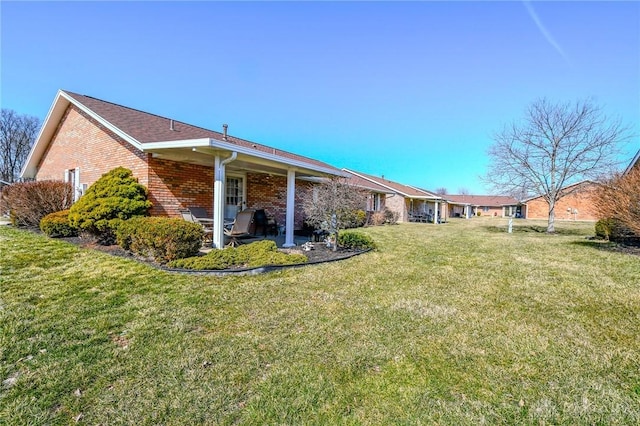 rear view of house with brick siding, a patio area, and a lawn