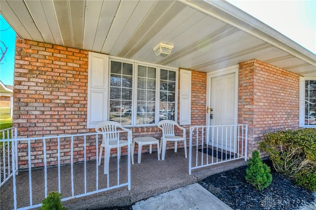 view of exterior entry featuring brick siding and covered porch