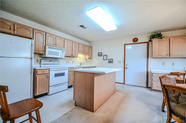 kitchen with light brown cabinets, white appliances, a center island, and light countertops