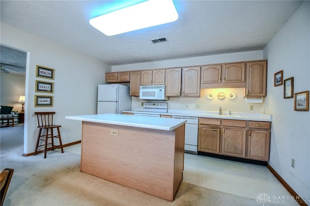 kitchen with visible vents, a sink, a center island, white appliances, and light countertops