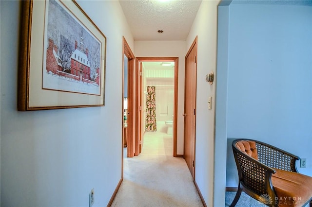 hallway with light colored carpet, baseboards, and a textured ceiling