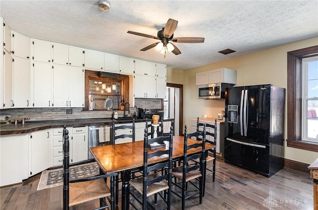 kitchen featuring dark wood-style floors, stainless steel appliances, white cabinetry, dark countertops, and tasteful backsplash