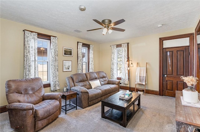 carpeted living area with baseboards, visible vents, a textured ceiling, and ceiling fan