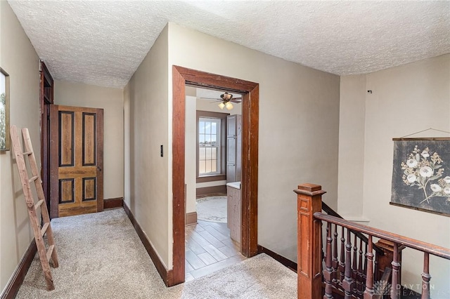 corridor with an upstairs landing, a textured ceiling, baseboards, and carpet floors