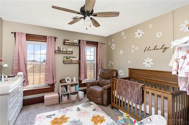 bedroom featuring a nursery area, multiple windows, light colored carpet, and a ceiling fan