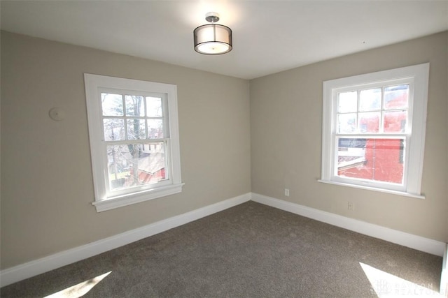 spare room featuring baseboards and dark colored carpet