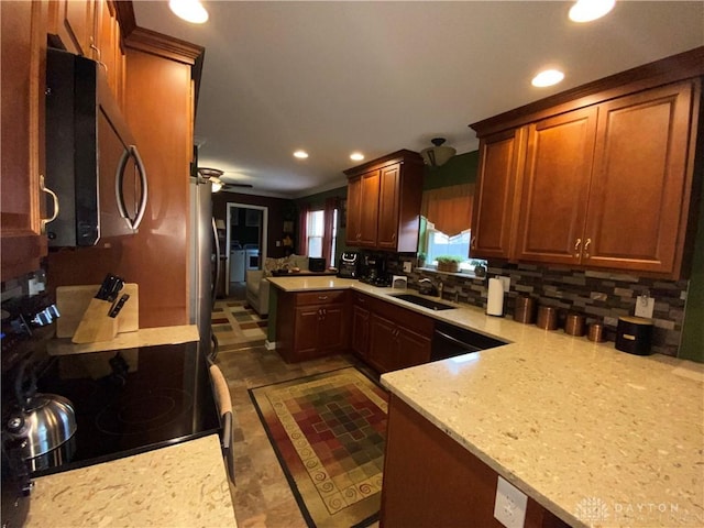 kitchen with a peninsula, ceiling fan, a sink, black appliances, and backsplash