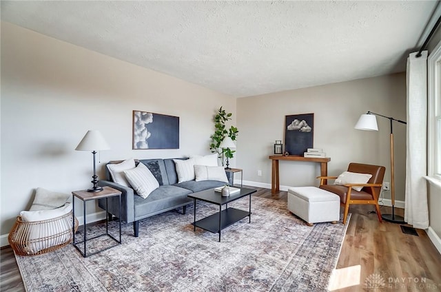 living room featuring a textured ceiling, baseboards, and wood finished floors