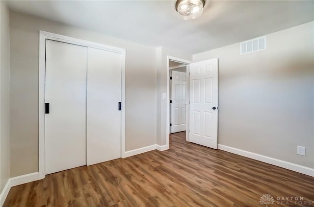 unfurnished bedroom with wood finished floors, visible vents, a closet, and baseboards