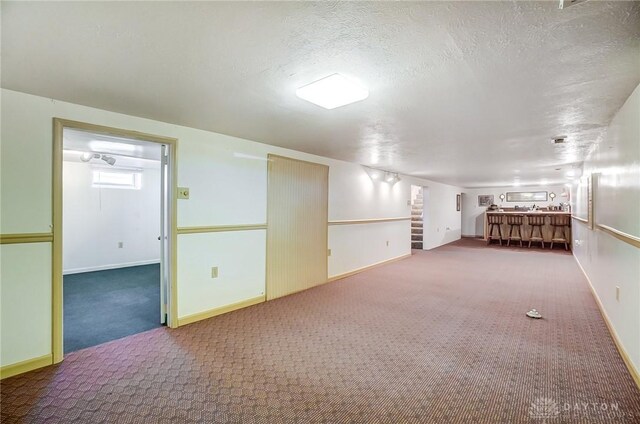 basement with carpet flooring, a textured ceiling, and baseboards