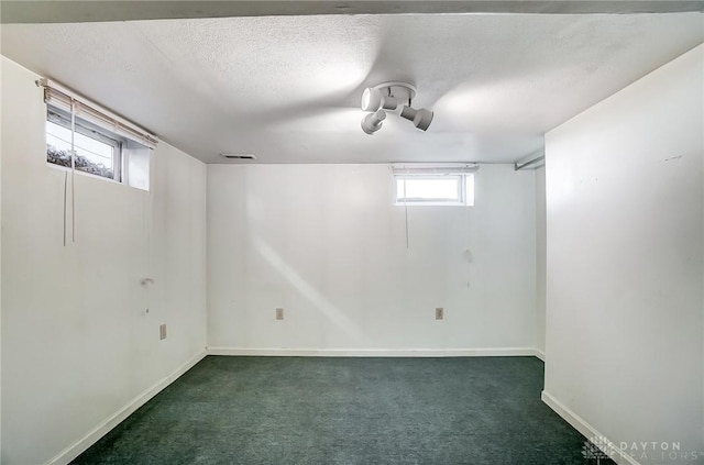 basement featuring baseboards, carpet, visible vents, and a textured ceiling