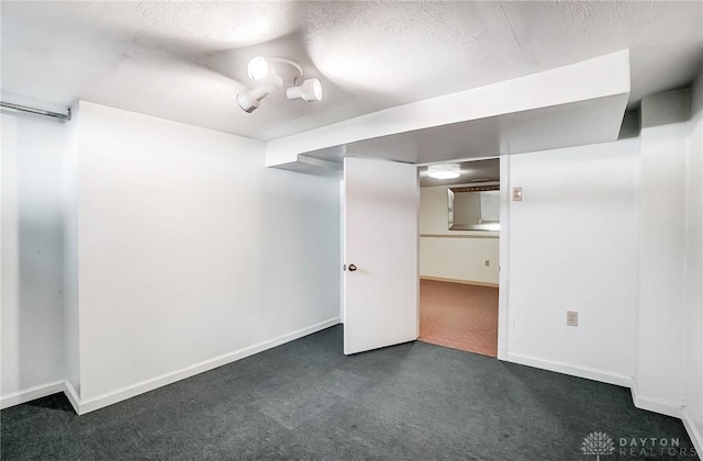 below grade area with dark carpet, a textured ceiling, and baseboards