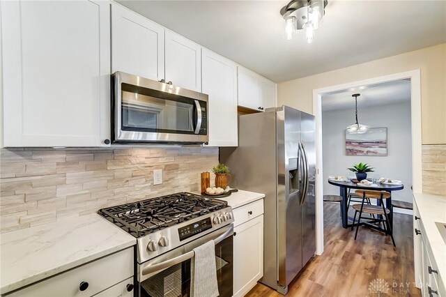 kitchen with light wood-style flooring, white cabinetry, appliances with stainless steel finishes, decorative backsplash, and light stone countertops