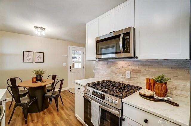 kitchen with white cabinets, backsplash, light wood-style floors, and appliances with stainless steel finishes