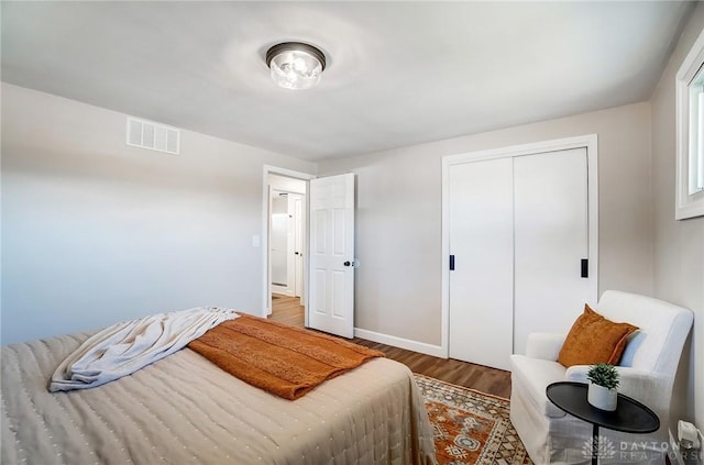 bedroom with a closet, visible vents, baseboards, and wood finished floors