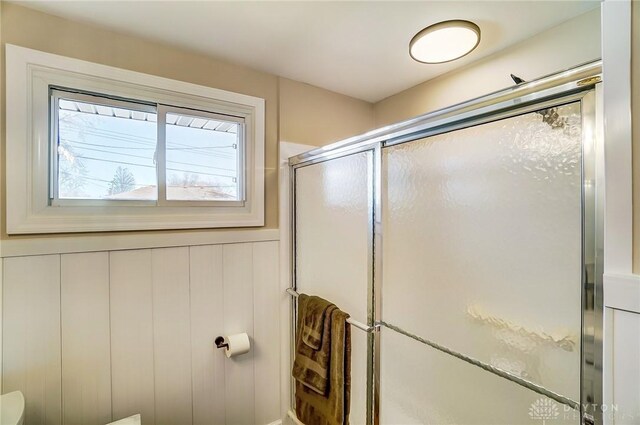 full bathroom with a shower stall and a wainscoted wall