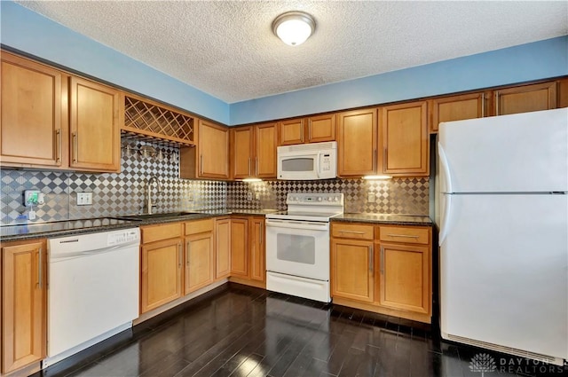 kitchen featuring dark countertops, dark wood finished floors, white appliances, and a sink