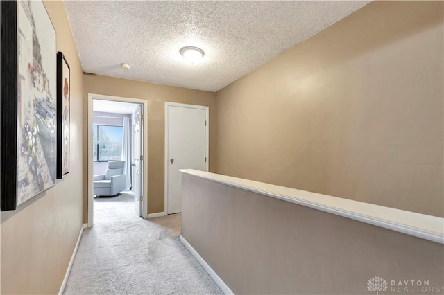 corridor featuring a textured ceiling, baseboards, and light carpet