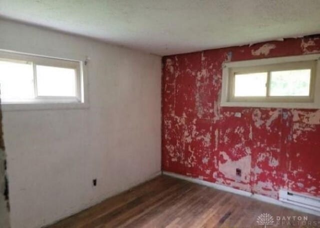 spare room with a healthy amount of sunlight, a baseboard radiator, baseboards, and wood finished floors