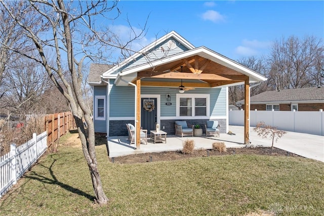 view of front of home with a front lawn, ceiling fan, a fenced backyard, stone siding, and a patio