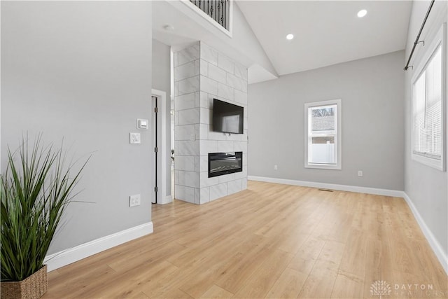 unfurnished living room featuring light wood-type flooring, high vaulted ceiling, recessed lighting, baseboards, and a tile fireplace