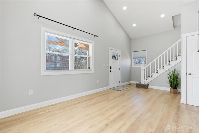 foyer featuring light wood-type flooring, stairway, baseboards, and high vaulted ceiling