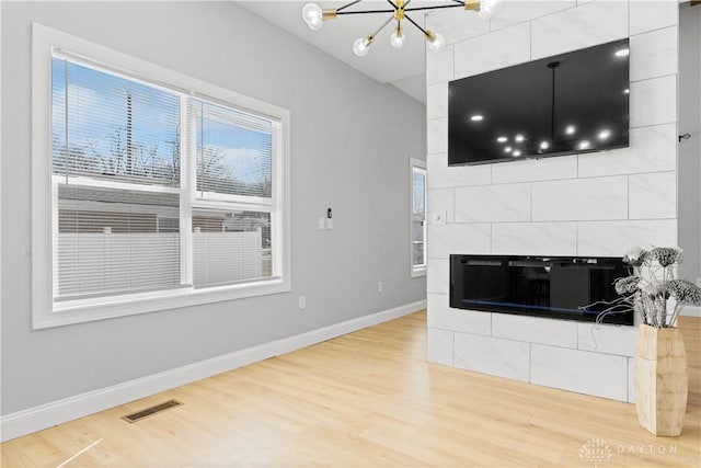 unfurnished living room featuring visible vents, baseboards, a chandelier, light wood-style flooring, and a fireplace