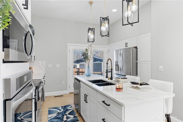 kitchen with a center island with sink, a sink, white cabinetry, light wood-style floors, and appliances with stainless steel finishes