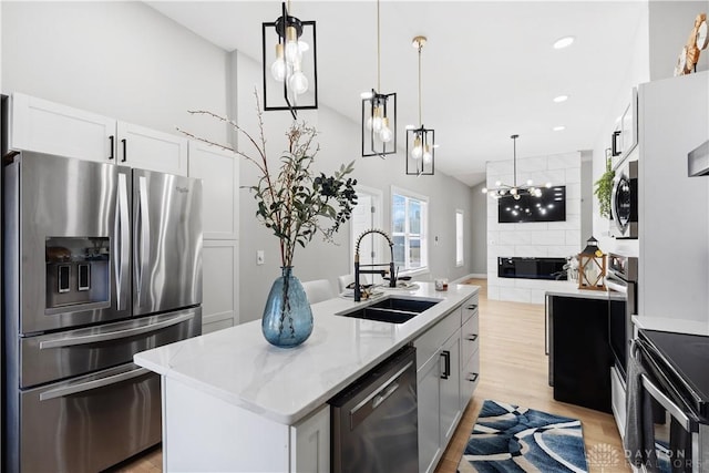 kitchen featuring light stone counters, a center island with sink, a sink, stainless steel appliances, and decorative light fixtures