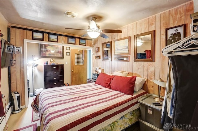 bedroom with visible vents, ceiling fan, wooden walls, and a baseboard radiator