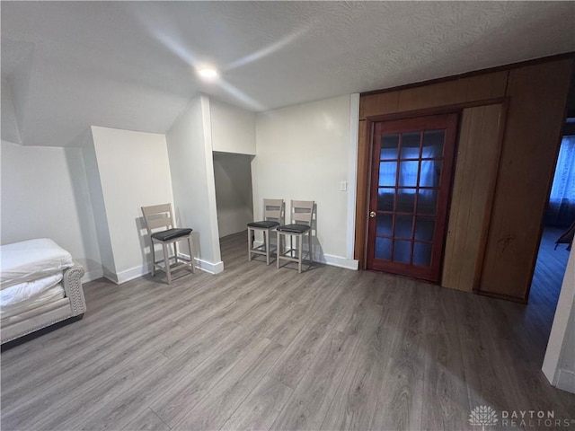 interior space with baseboards, a textured ceiling, wood finished floors, and vaulted ceiling