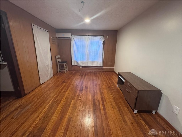 unfurnished bedroom featuring a textured ceiling, a wall unit AC, and wood finished floors