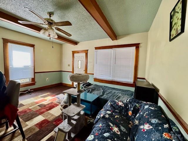 living room with baseboards, beam ceiling, a textured ceiling, and a ceiling fan