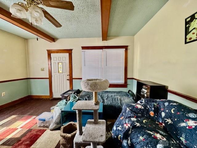 interior space featuring beam ceiling, a textured ceiling, baseboards, and wood finished floors