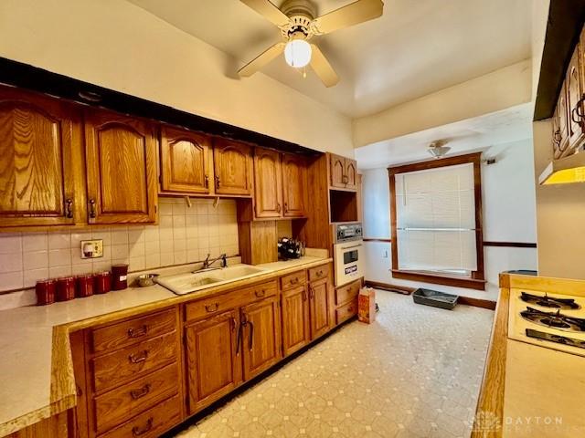 kitchen featuring light countertops, decorative backsplash, brown cabinets, white oven, and a sink