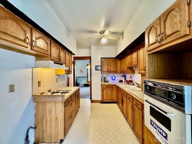 kitchen with white appliances, a ceiling fan, a sink, light countertops, and under cabinet range hood