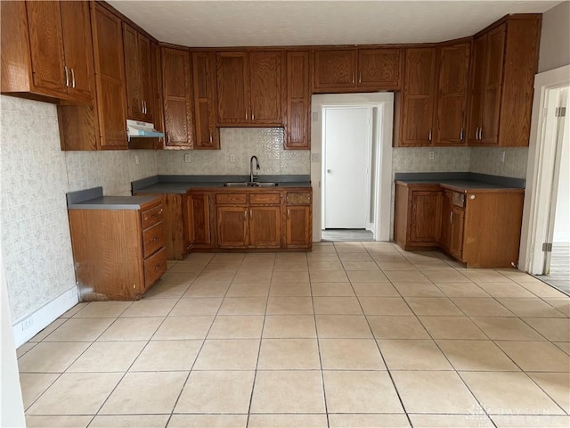 kitchen featuring brown cabinets, under cabinet range hood, a sink, light tile patterned floors, and decorative backsplash