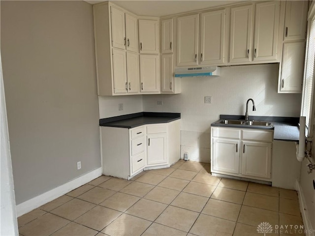 kitchen with dark countertops, baseboards, under cabinet range hood, light tile patterned flooring, and a sink