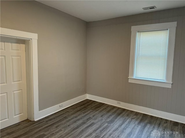 empty room with dark wood finished floors, visible vents, and baseboards