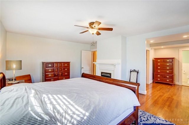 bedroom featuring light wood-type flooring, baseboards, ceiling fan, and a fireplace