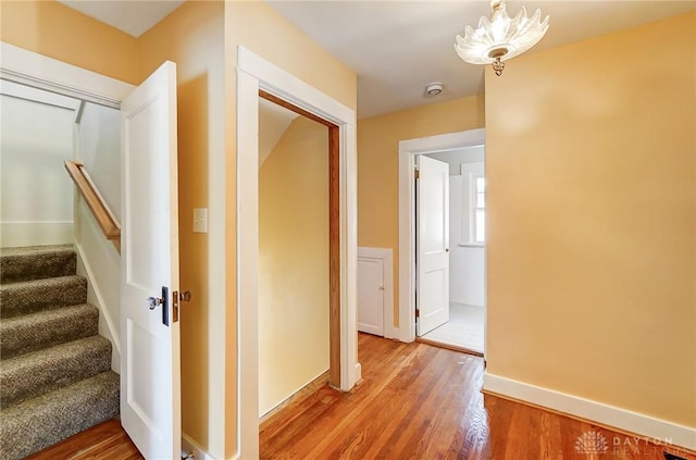 hallway featuring a notable chandelier, light wood-style flooring, stairs, and baseboards