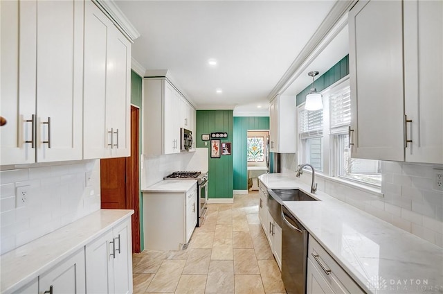 kitchen featuring a sink, appliances with stainless steel finishes, white cabinets, crown molding, and light stone countertops