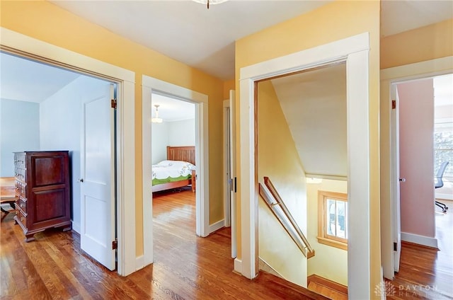 corridor with baseboards, an upstairs landing, and wood finished floors