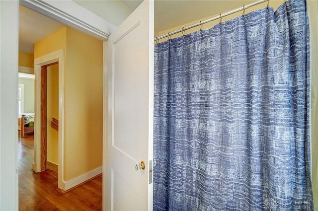 bathroom featuring a shower with curtain, baseboards, and wood finished floors