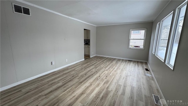 empty room featuring visible vents, baseboards, light wood-style floors, and crown molding